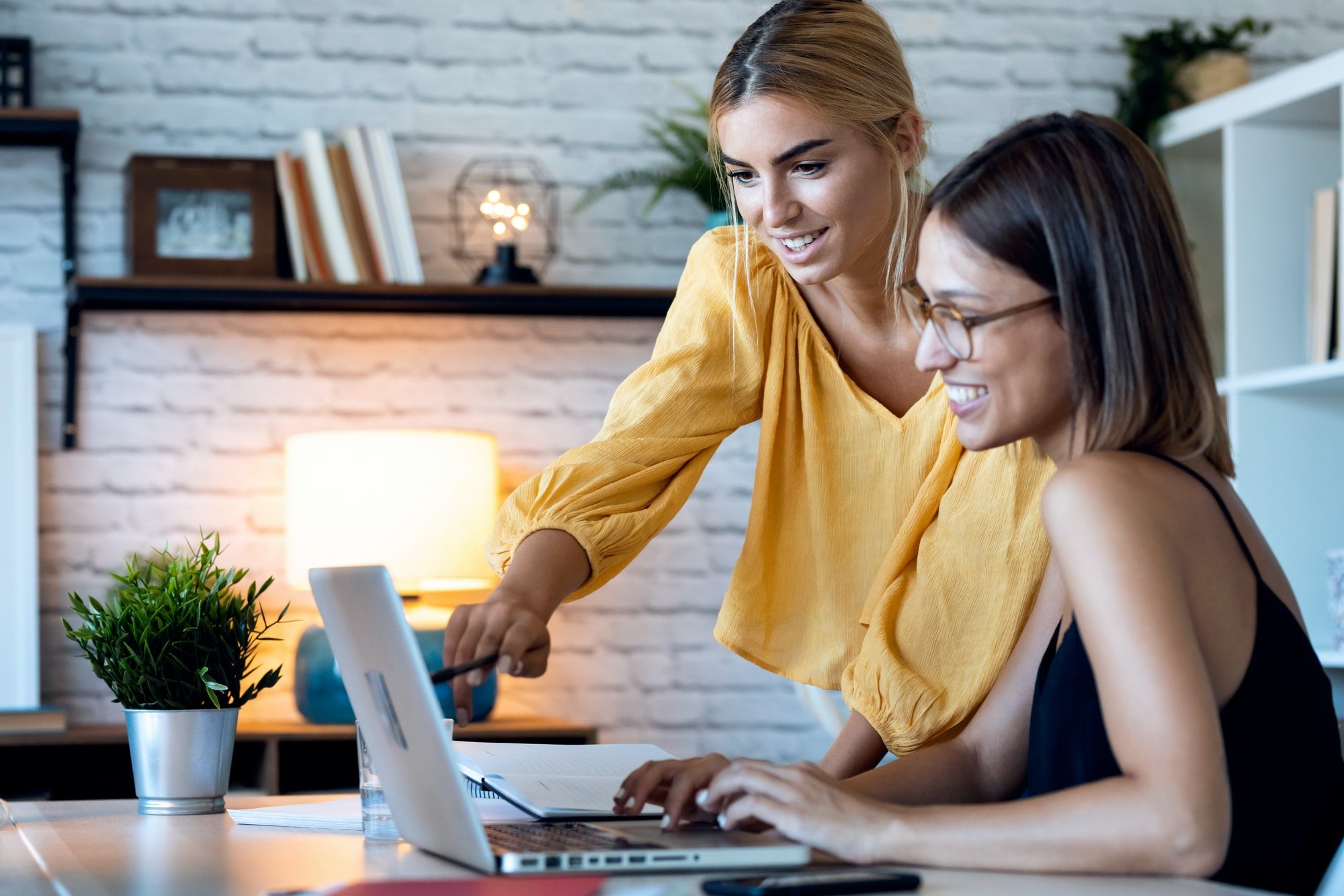 Dua wanita sedang mengerjakan laptop di kantor.