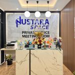 Area resepsionis di Nustara Space dengan meja marmer, rangkaian bunga warna-warni, dan papan bertuliskan "Private Office Meeting Room" di dinding belakang.