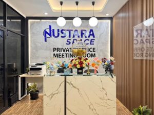 Area resepsionis di Nustara Space dengan meja marmer, rangkaian bunga warna-warni, dan papan bertuliskan "Private Office Meeting Room" di dinding belakang.