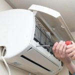 Seseorang menggunakan obeng untuk memperbaiki atau merawat unit AC yang terpasang di dinding.